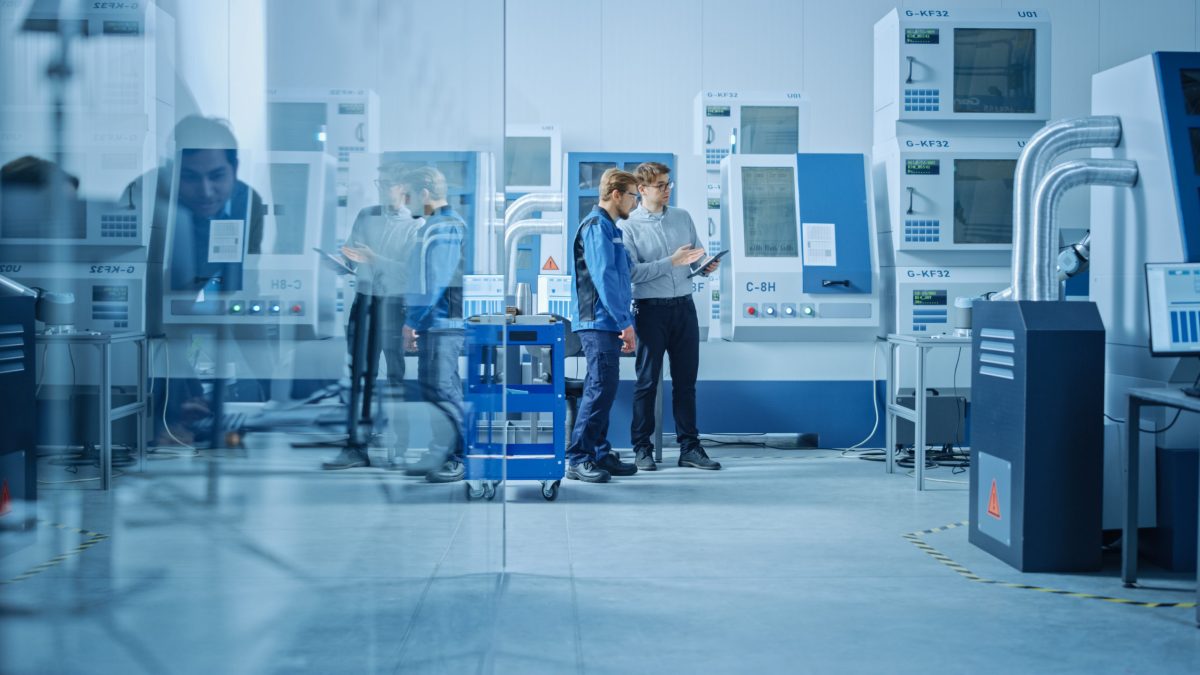 Works discuss next steps while surrounded by high-tech factory equipment.