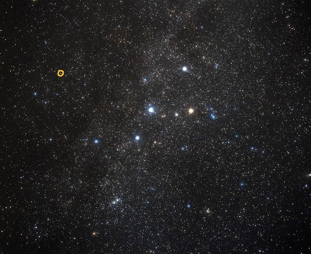 A dense field of stars in the night sky with a small yellow circle highlighting a specific star near the upper left corner.