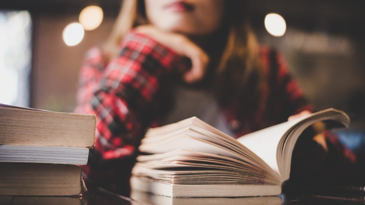 A woman stares pensively while reading a book.