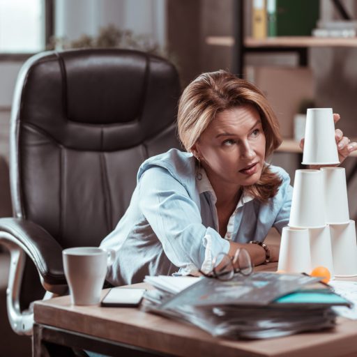 A woman with no inspiration stacks cups on her desk.