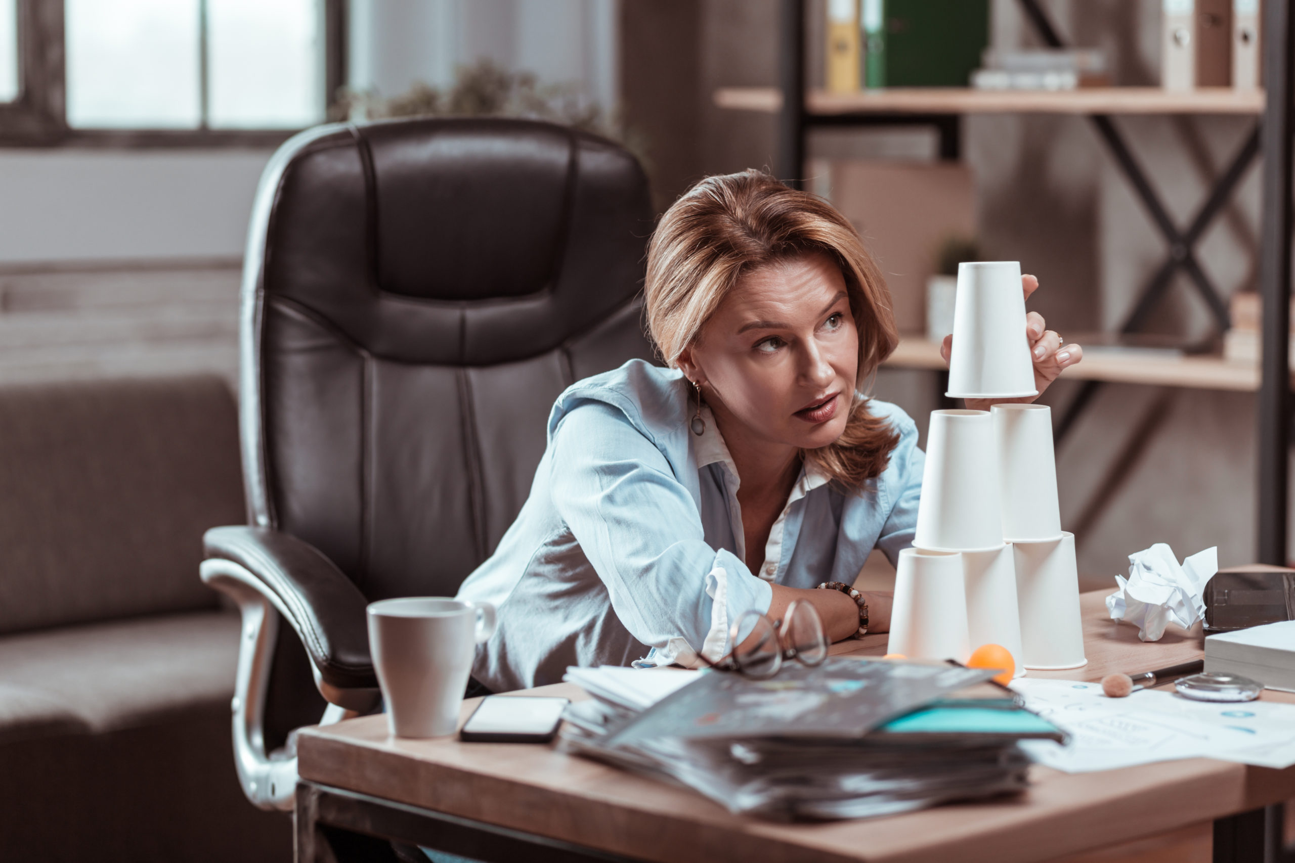 A woman with no inspiration stacks cups on her desk.
