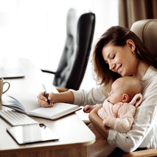 A working mom makes notes while holding her daughter.