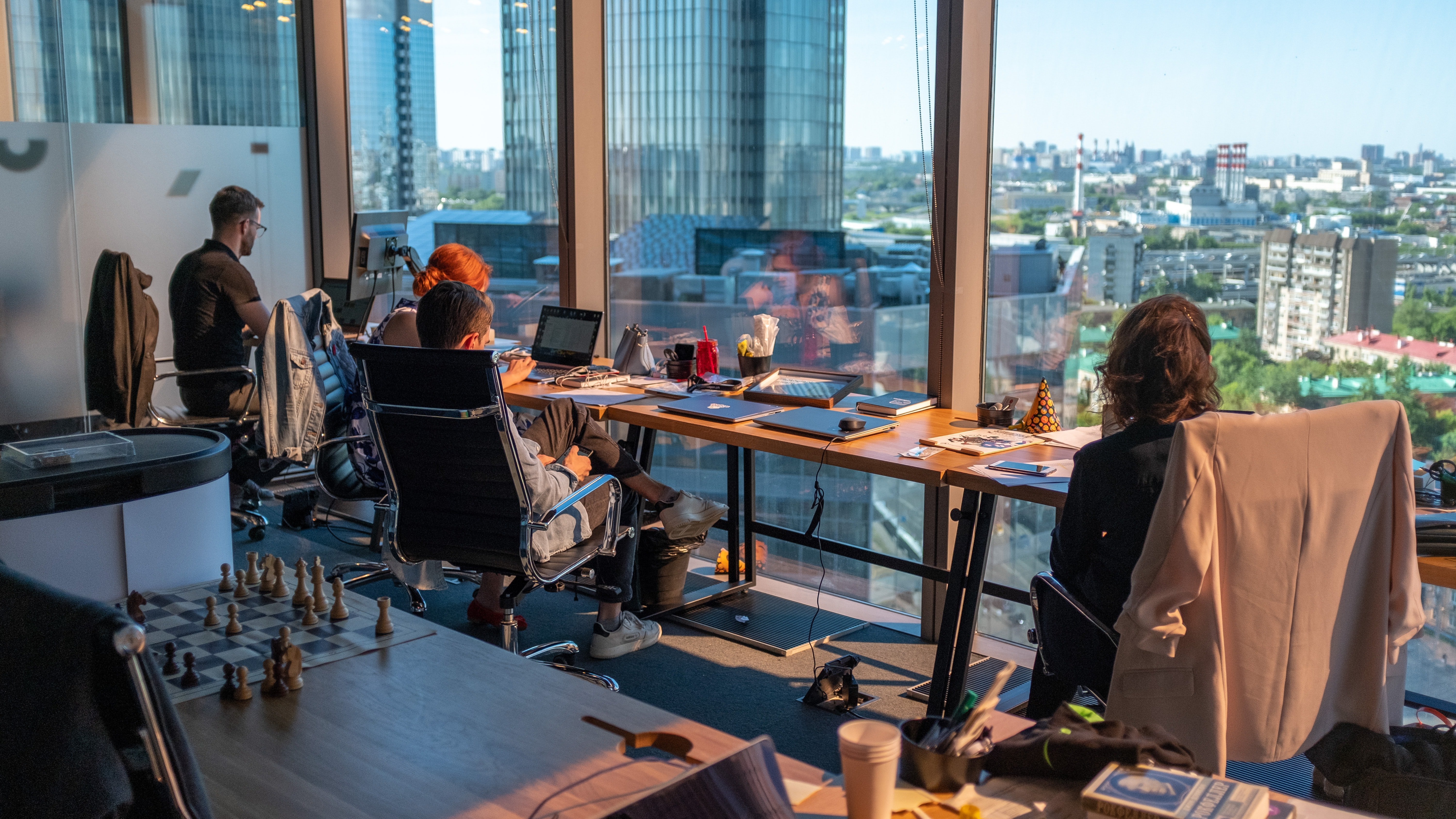 The future of work illustrated by four colleagues sitting at a long table by a window.