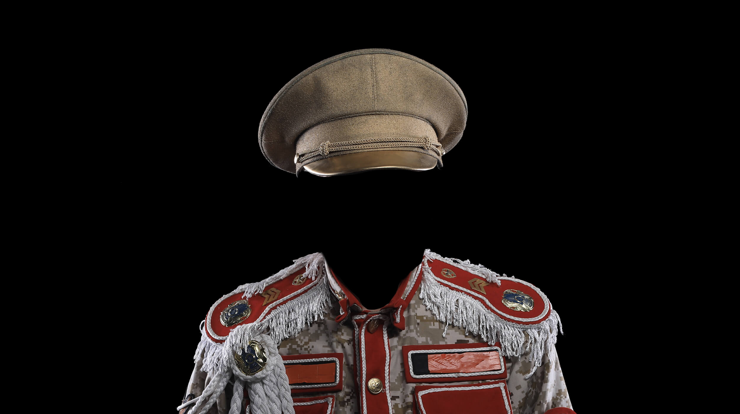 A military-style, decorated uniform and cap with no visible wearer, set against a solid black background, evokes powerful imagery that prompts viewers to consider themes such as authority and questions like what is fascism.