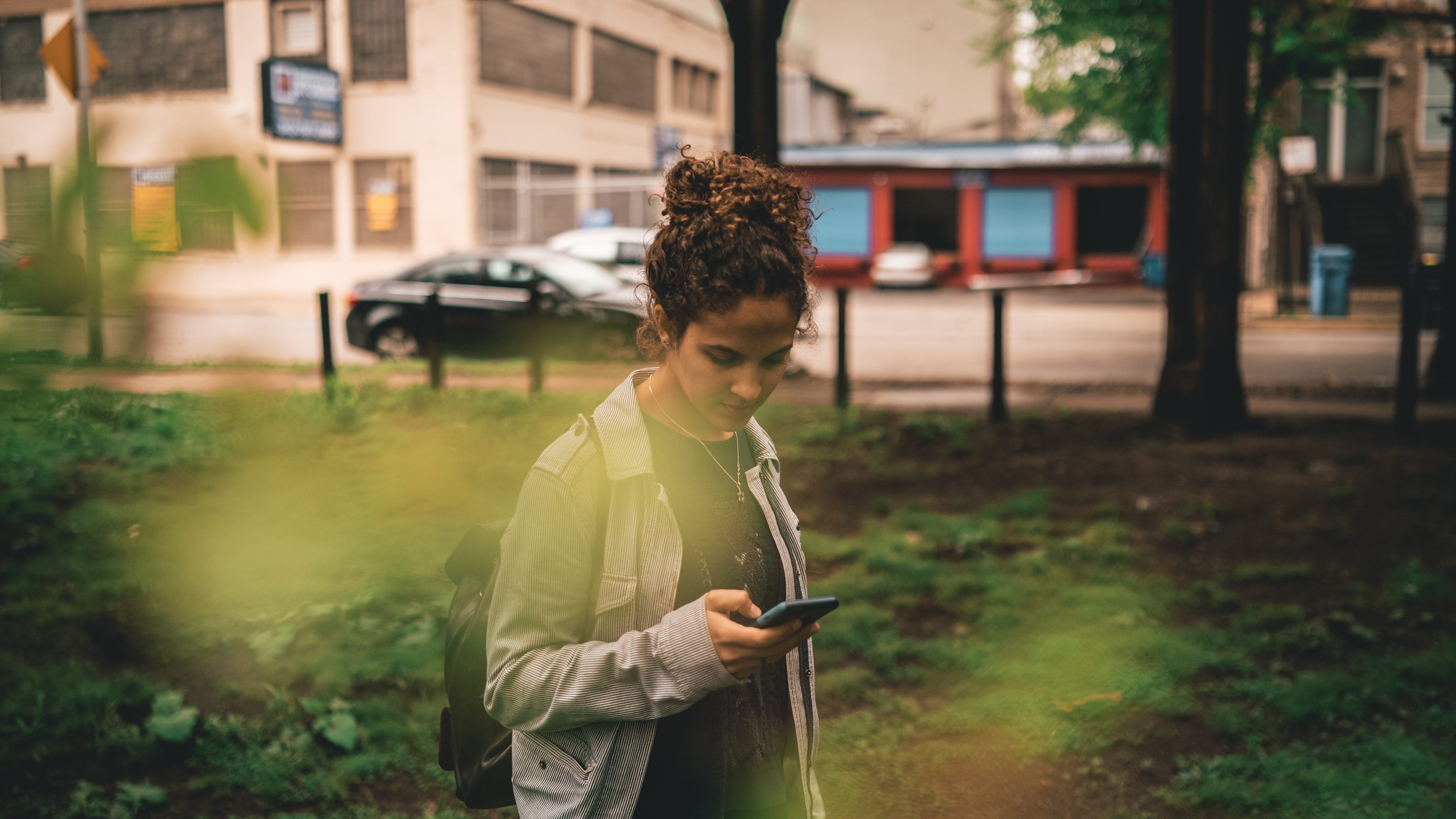 A young woman looks at her phone outside.