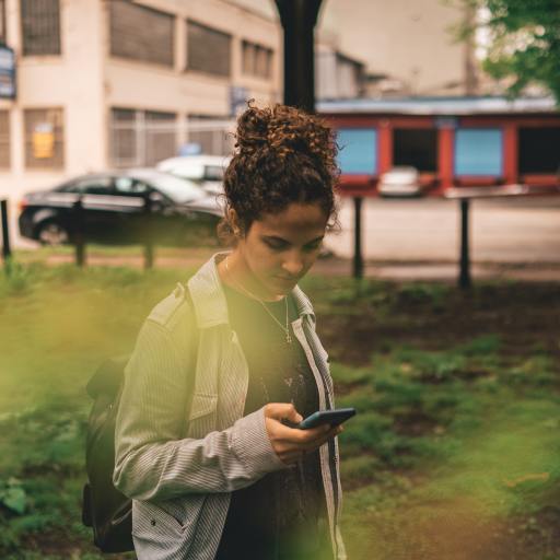 A young woman looks at her phone outside.