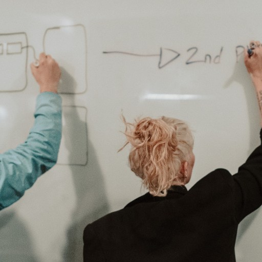 A man and a woman drawing on a white board for an article on how your personality type affects your salary.
