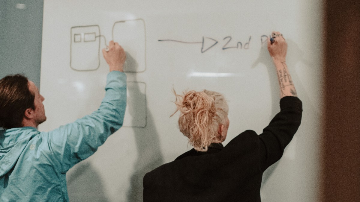 A man and a woman drawing on a white board for an article on how your personality type affects your salary.