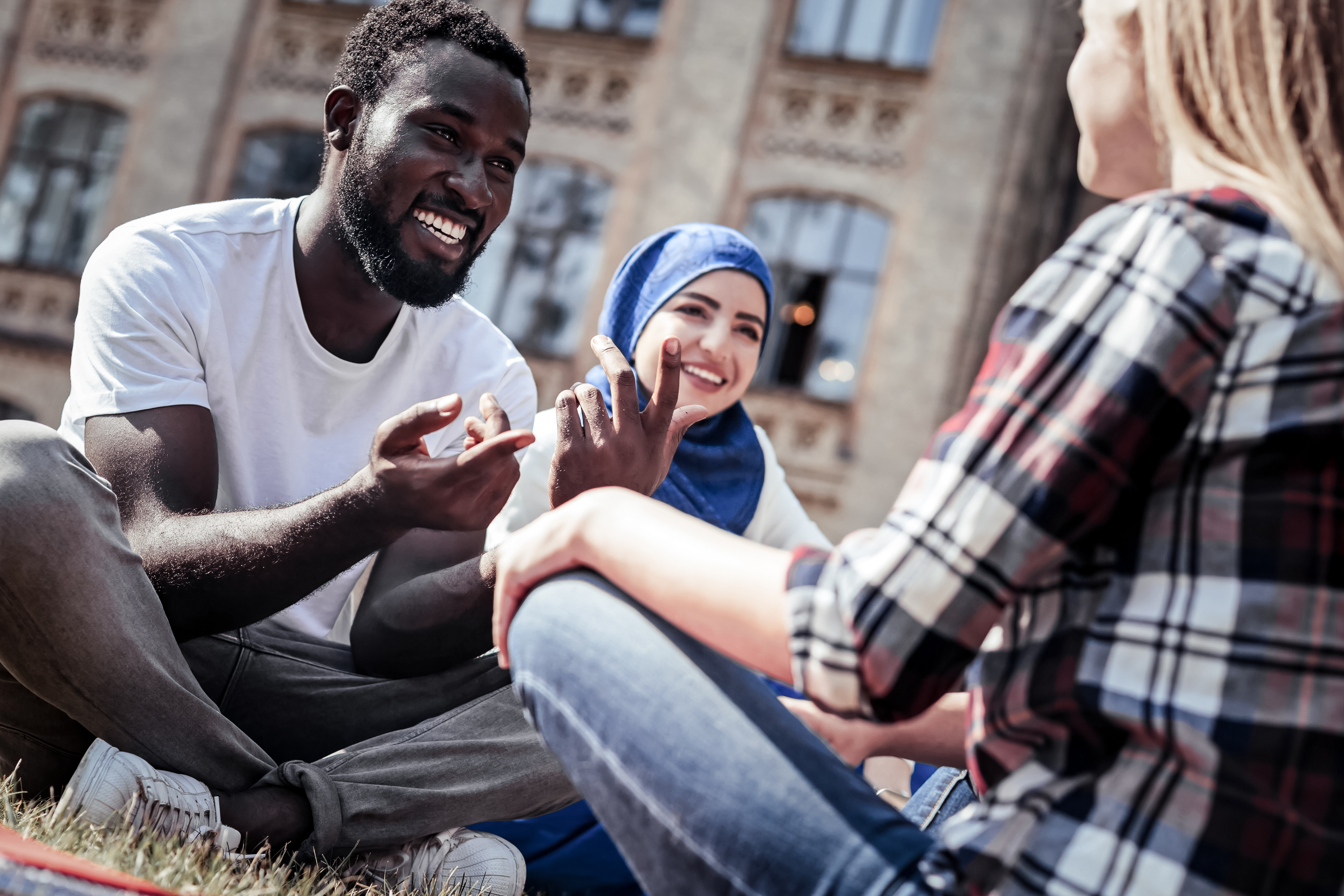 A man has a conversation with two women on a college green.