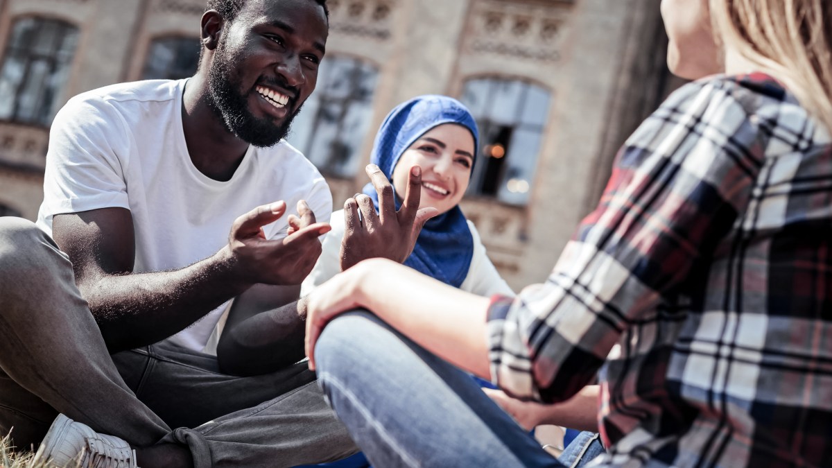 A man has a conversation with two women on a college green.