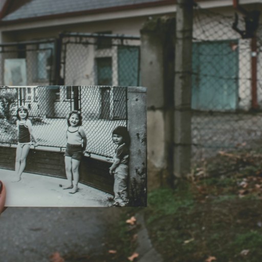 A hand holding an old photo of three girls over the present day location.