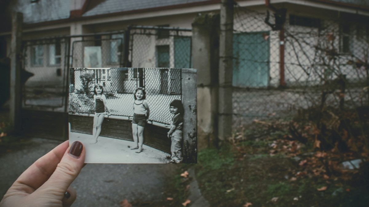 A hand holding an old photo of three girls over the present day location.