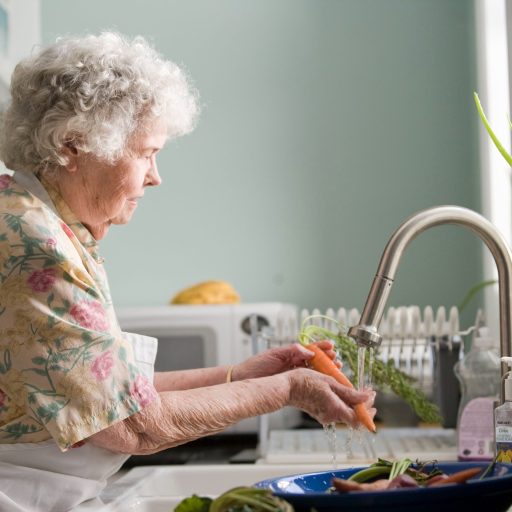 An elderly woman washing vegetables in a sink.