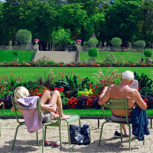 An older man and woman sunbathing in garden chairs.