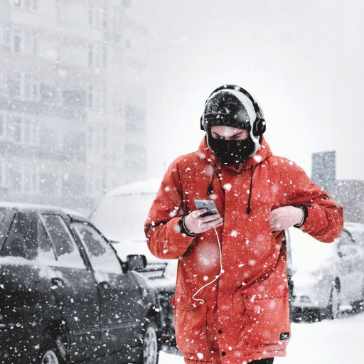 A man walks through the snow listening to music on his headphones.