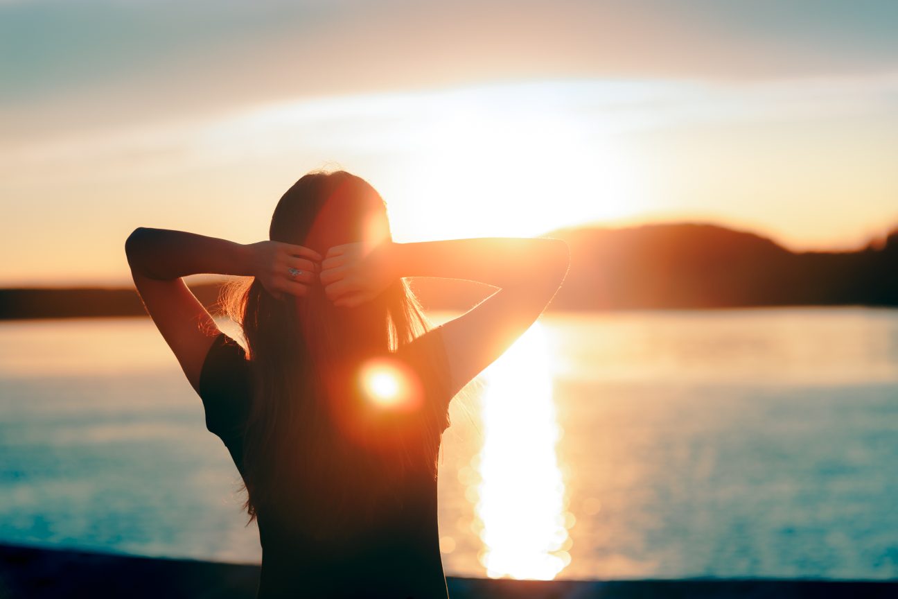 A woman looks at the sunset by the sea.