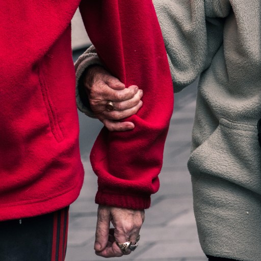 Two older adults linking arms while walking.