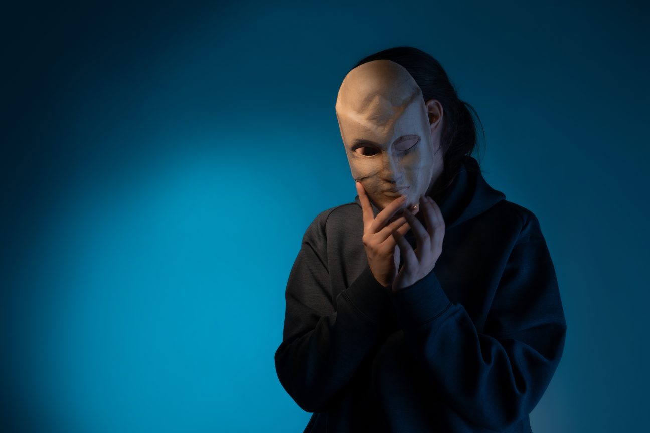 A young woman hides behind a mask