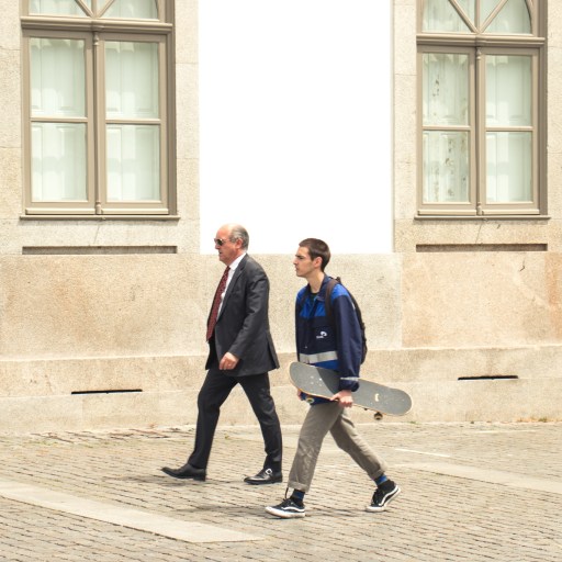 A man in a suit walks next to a teenage boy carrying a skateboard, illustrating life stages.