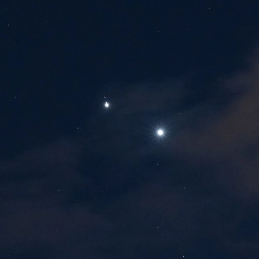 Two bright celestial objects, including the brightest planet, shine in the night sky, partially obscured by clouds and surrounded by smaller, faint stars.