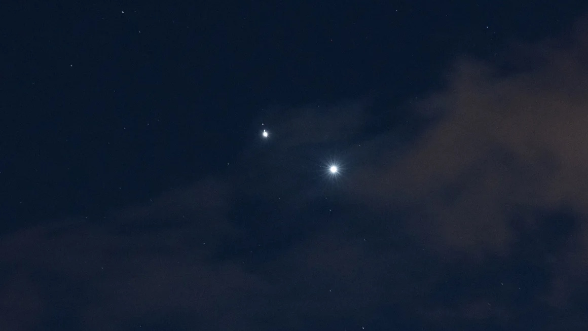 Two bright celestial objects, including the brightest planet, shine in the night sky, partially obscured by clouds and surrounded by smaller, faint stars.