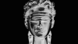 A metallic, blindfolded bust of a person is shown against a black background, symbolizing justice, impartiality, and the resolve to turn the other cheek in the face of adversity.