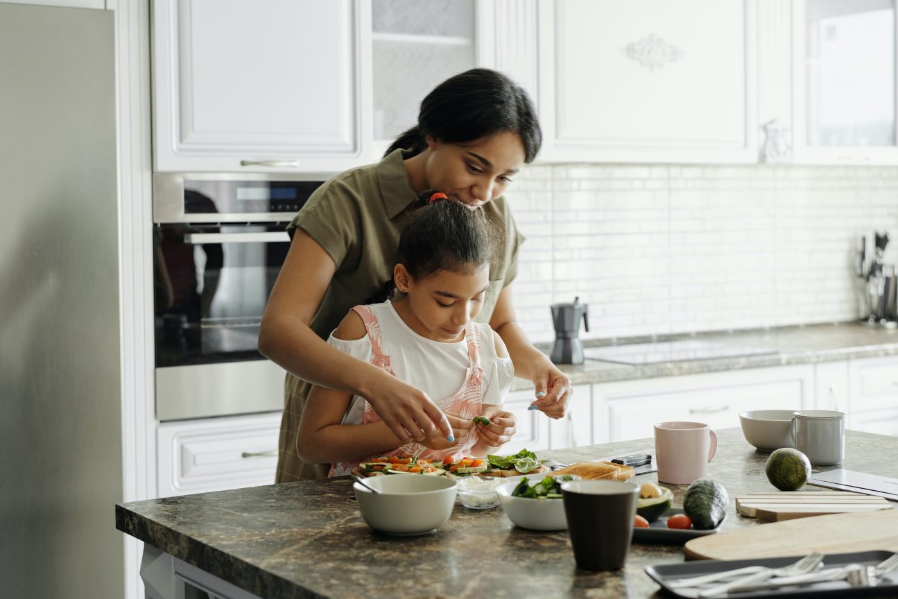A mother and daughter prepare avocado toast in the kitchen.