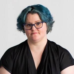a woman with blue hair and glasses posing for a picture.