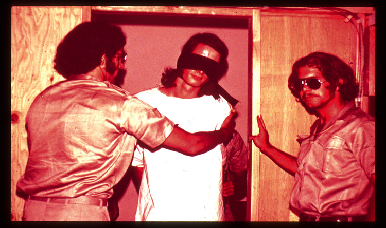 Participants given the role of guards during the Stanford Prison Experiment lead a blindfolded participant who was given the role of prisoner.