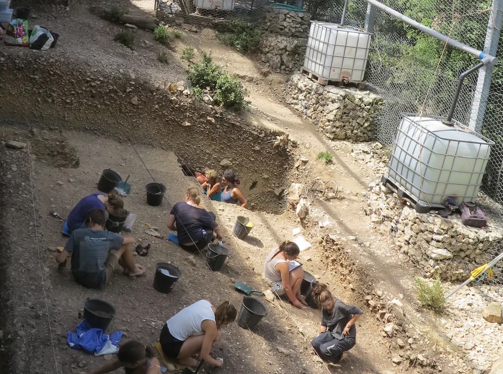a group of people sitting on the ground next to a fence.