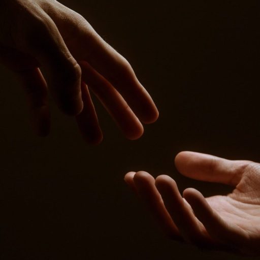 two hands reaching towards each other in the dark.