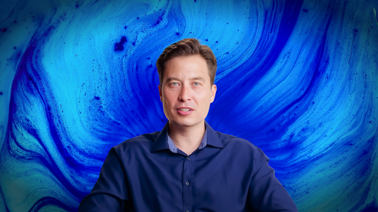 A man in a blue shirt sits in front of a vivid blue and turquoise swirling abstract background.