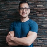 a man wearing glasses standing in front of a brick wall.