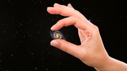 A hand pinches a small spiral galaxy between its fingers against a background of stars in space.