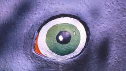 Close-up of a painted eye on a textured surface, featuring green, white, black, and a small area of orange.