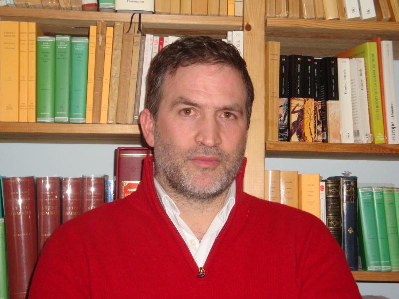 a man in a red sweater standing in front of a bookshelf.