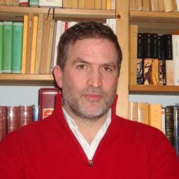 a man in a red sweater standing in front of a bookshelf.