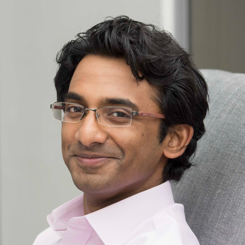 Person wearing glasses, smiling slightly, seated in a chair, with a neutral background.
