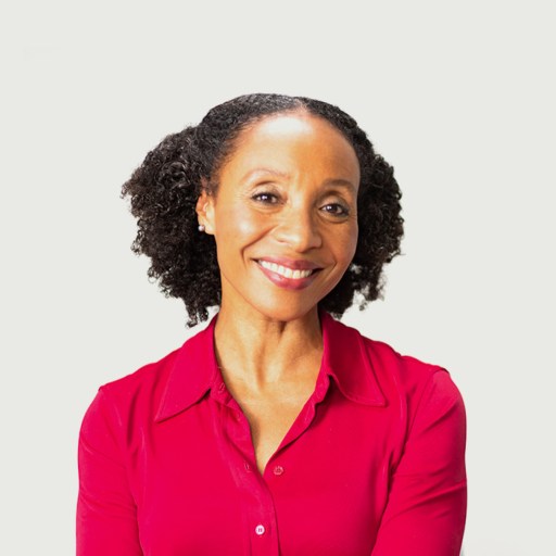 A woman with curly hair, wearing a red blouse, smiles at the camera against a plain white background.