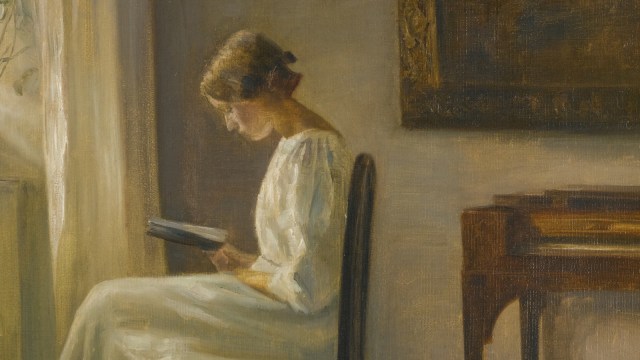 A woman in a white dress sits on a chair by a window, reading a book in a softly lit room with a piano nearby, embodying the quiet charm of why read old books.