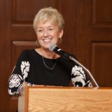 A woman smiles at a podium while giving a speech.