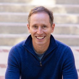 a smiling man sitting in front of some steps.