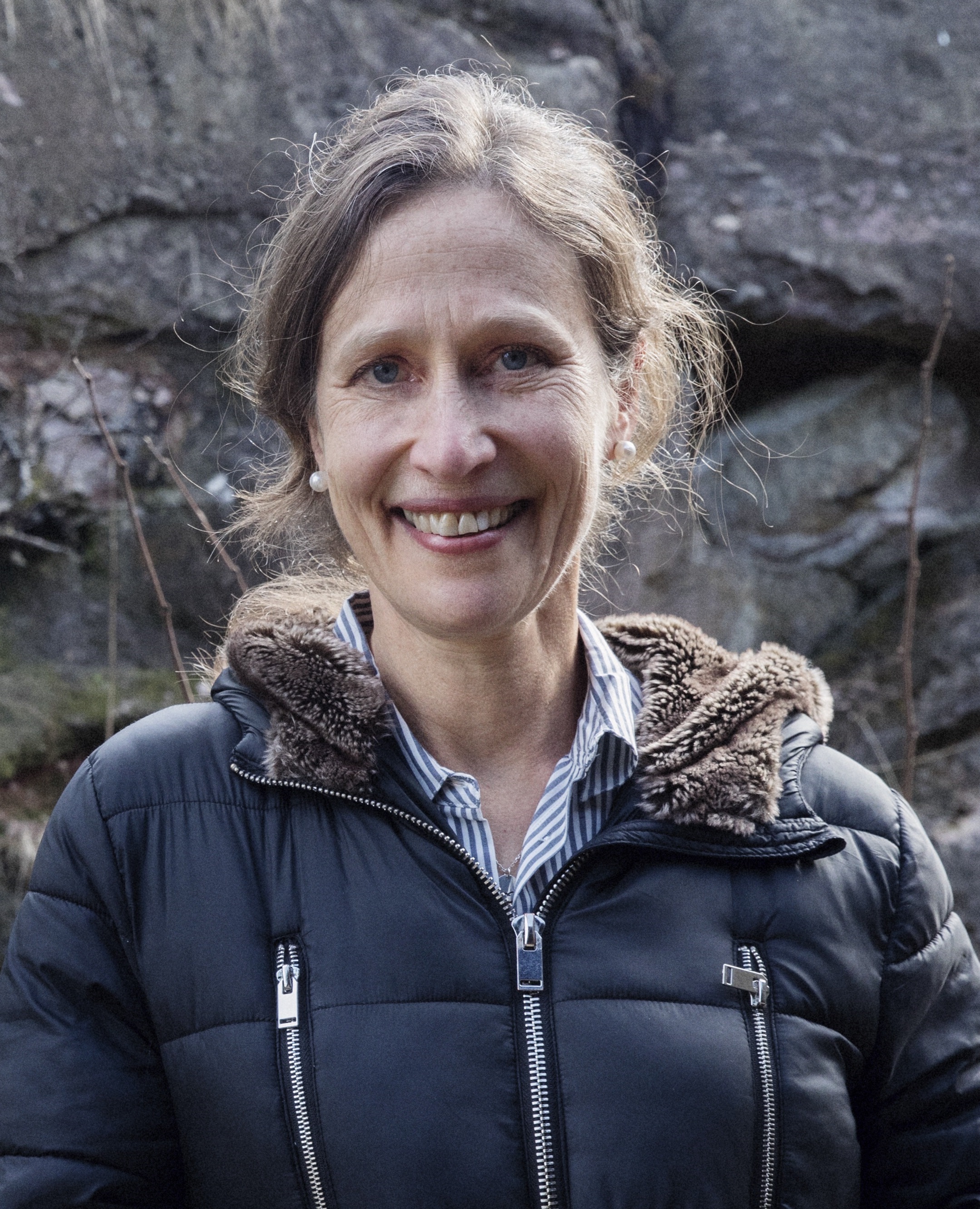 a woman in a black jacket standing in front of a rock.