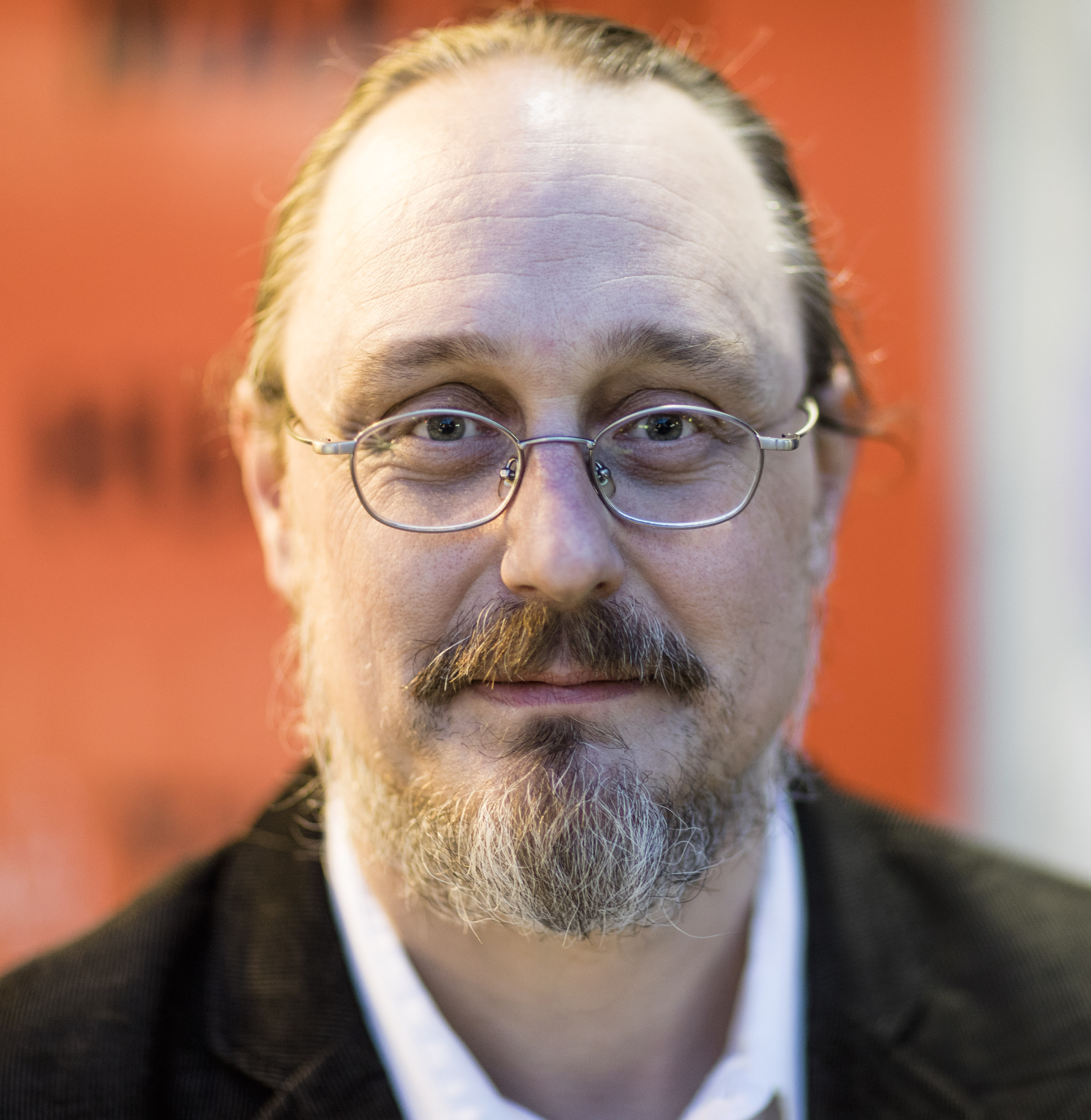 a man with glasses and a beard wearing a suit.