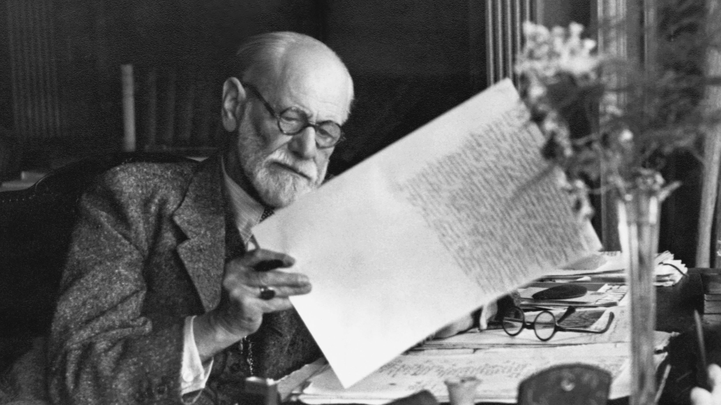 an old man sitting at a desk reading a book.