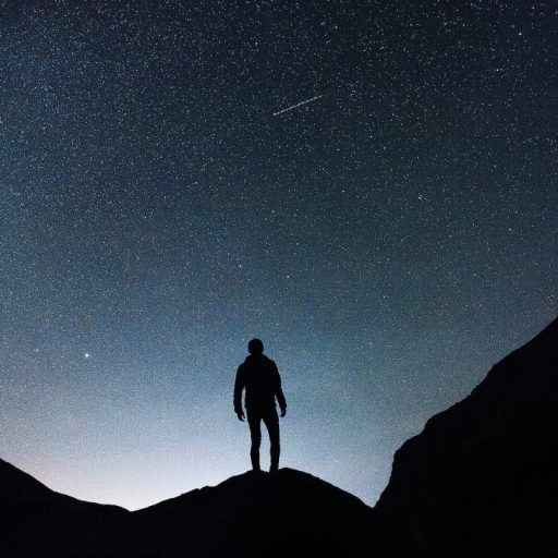 a person standing on top of a mountain under a starry sky.