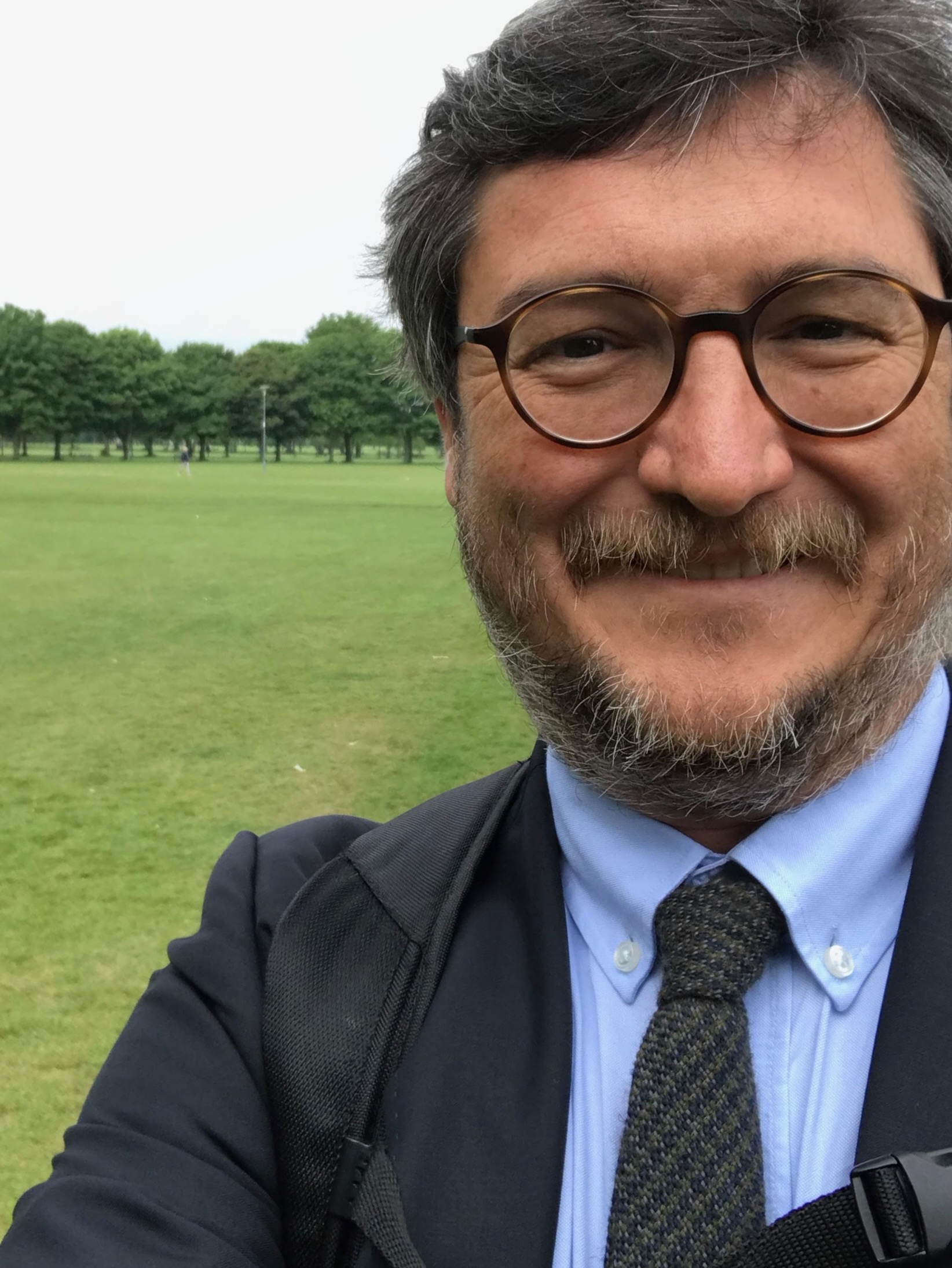 a man in a suit and tie is taking a selfie in a park.