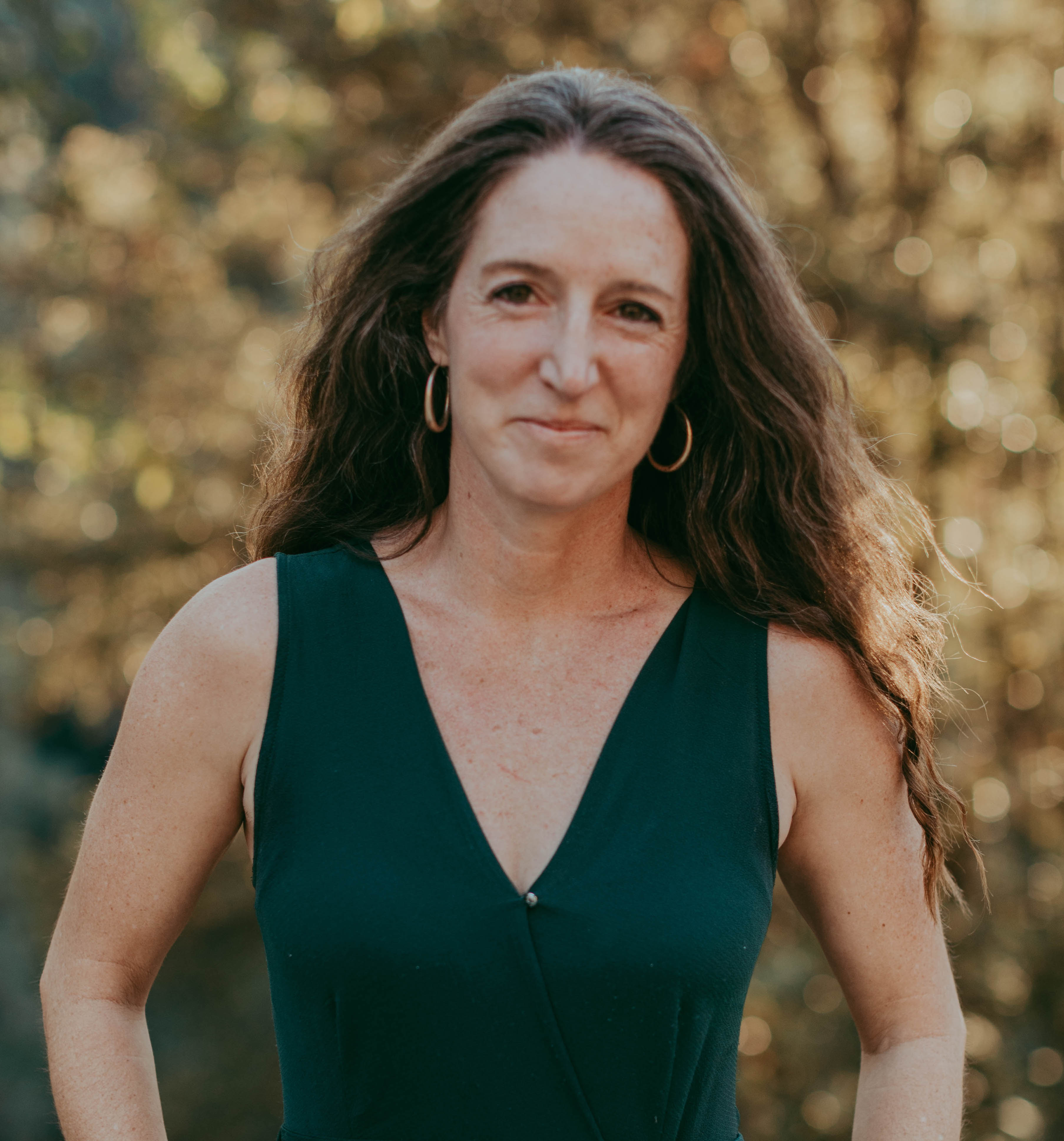 A woman in a green dress standing in front of trees.