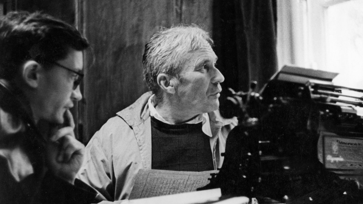 Two men sitting in front of a modern typewriter.