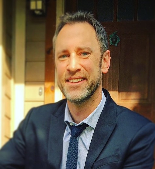 A man in a suit and tie smiling in front of a door.